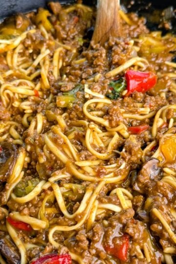 Close-up shot showing saucy Mongolian ground beef noodles with red peppers, mushrooms, and bits of green vegetables, highlighting the glossy, caramelized texture of the sauce.