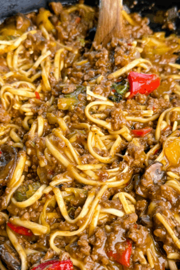 Close-up shot showing saucy Mongolian ground beef noodles with red peppers, mushrooms, and bits of green vegetables, highlighting the glossy, caramelized texture of the sauce.