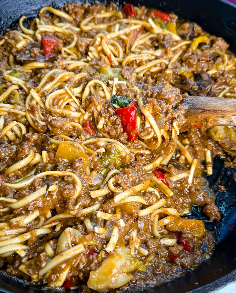 Close-up shot showing saucy Mongolian ground beef noodles with red peppers, mushrooms, and bits of green vegetables, highlighting the glossy, caramelized texture of the sauce.