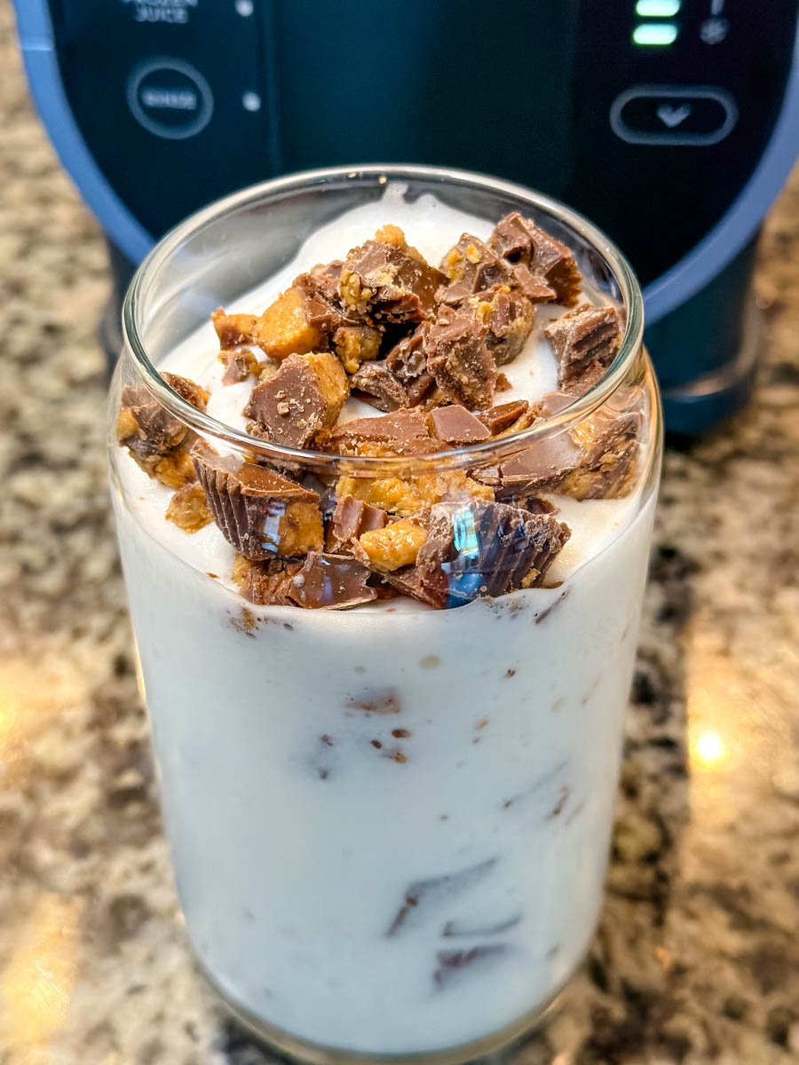 A glass filled with milk and chopped peanut butter cups before mixing, sitting on a granite countertop with the Ninja Slushi machine in the background.