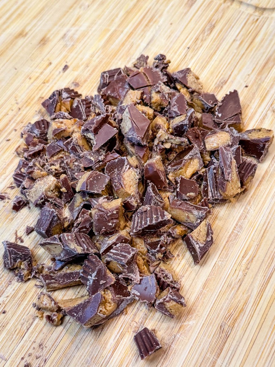 Chopped peanut butter cups on a wooden cutting board, with small and large chunks scattered across the surface.