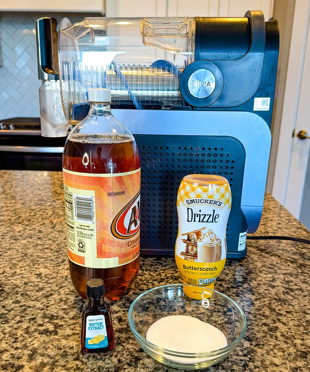 The full ingredient lineup for the recipe, including cream soda, butterscotch drizzle, sugar, butter extract, and a Ninja Slushi machine in the background.