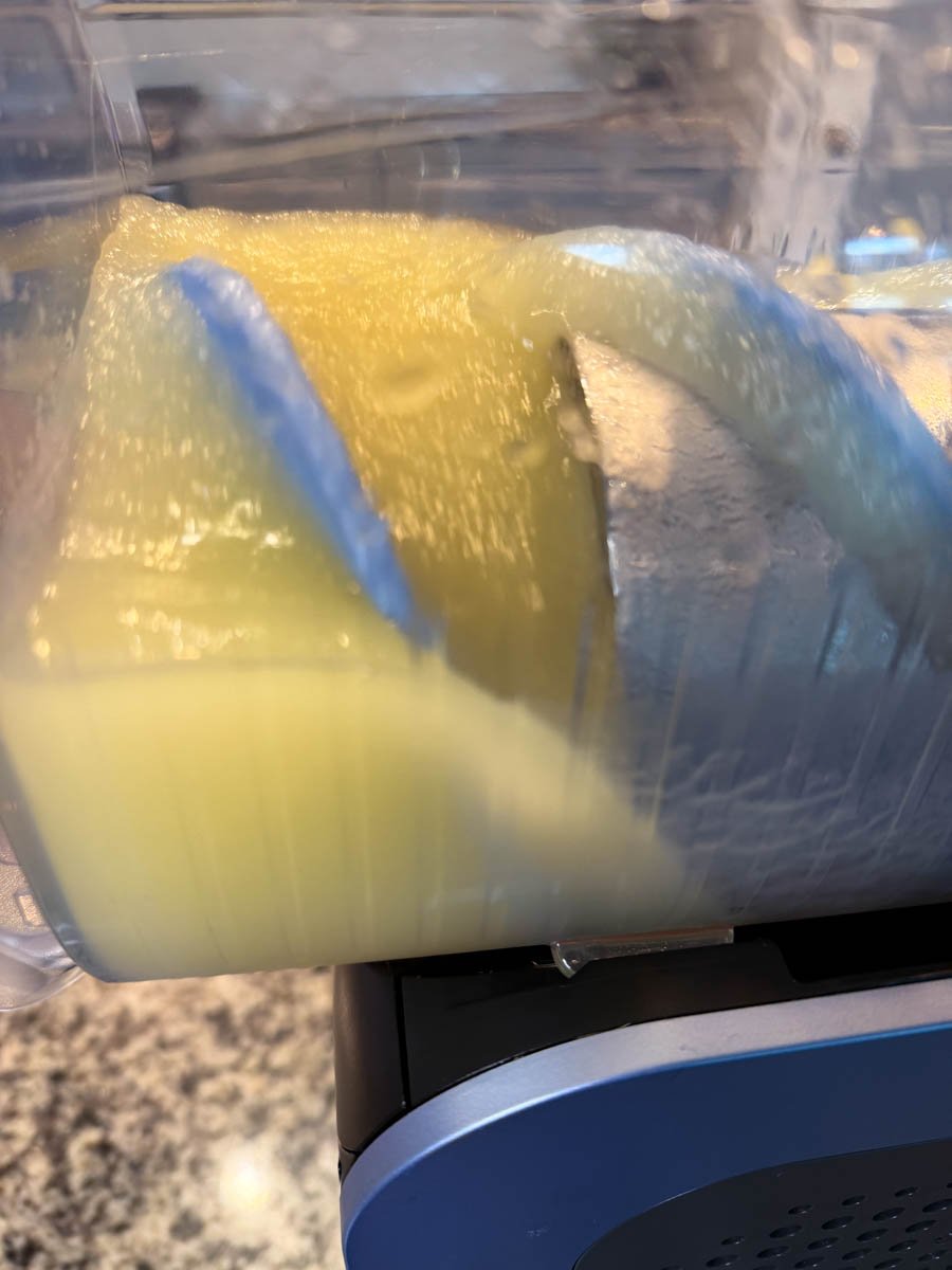 Inside the Ninja slushi machine showing the lemon drop mixture partially frozen, with the rotating paddle blending the icy lemon slush.