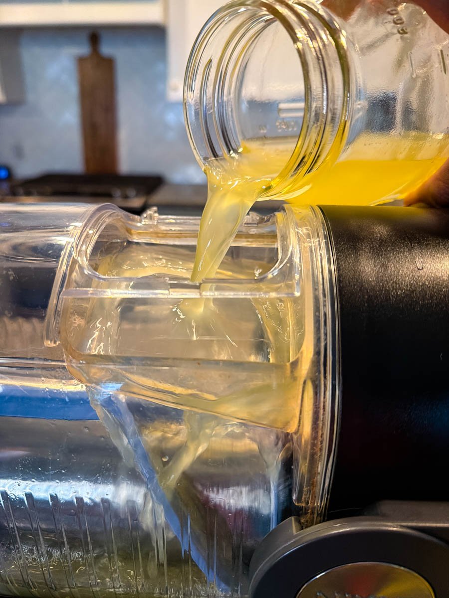 A jar of lemon mixture being poured into the top of the Ninja slushi machine, with the yellow liquid running down into the canister.