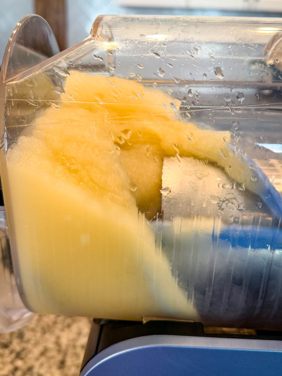 Close-up view inside the Ninja Slushi machine showing the Mai Tai mixture beginning to freeze into a thick, pale orange slush.