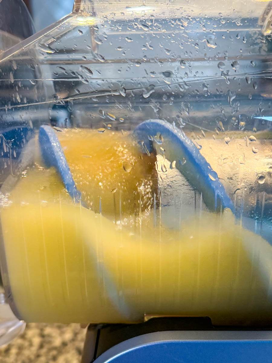Mai Tai mixture further along in the freezing process inside the Ninja Slushi machine, with the rotating paddle moving through the icy orange slush.