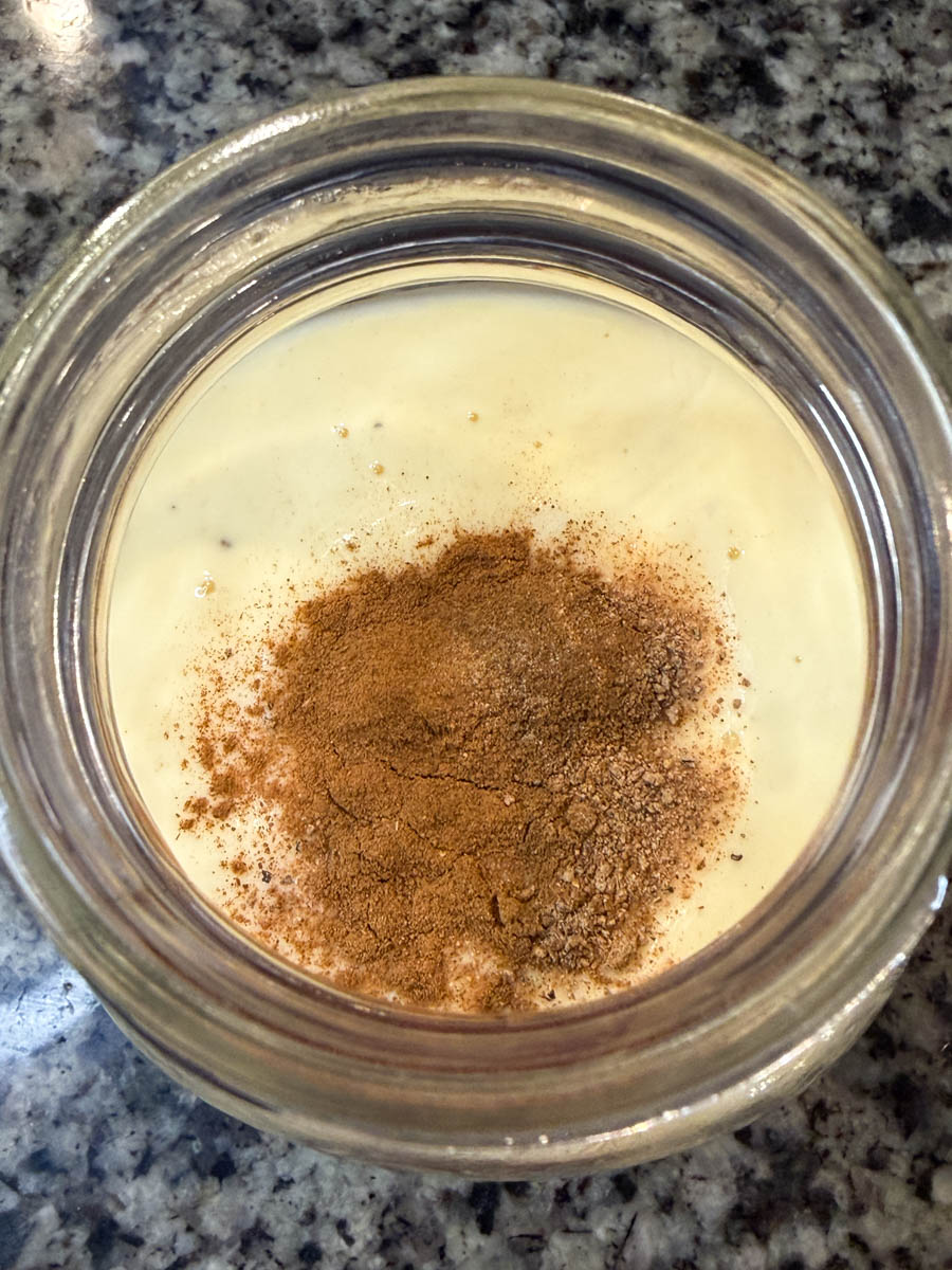 Overhead view of a mason jar with eggnog topped with ground cinnamon and nutmeg before mixing.