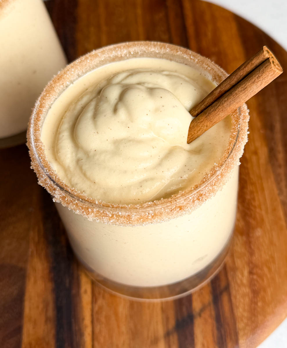 Close-up of a single glass of spiked eggnog showing the smooth, frozen texture and cinnamon sugar rim with a cinnamon stick garnish.