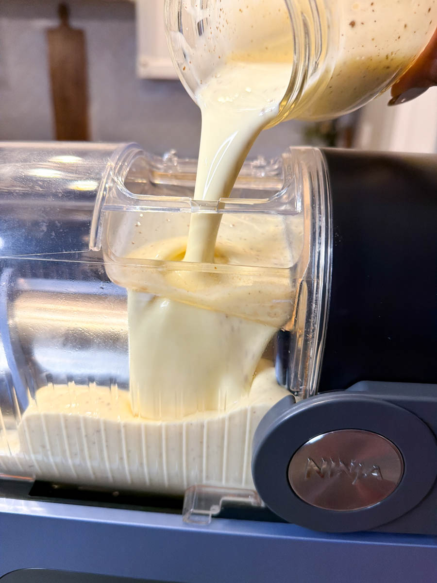 Smooth eggnog mixture being poured from a jar into the Ninja Slushi machine, filling the container with the creamy liquid