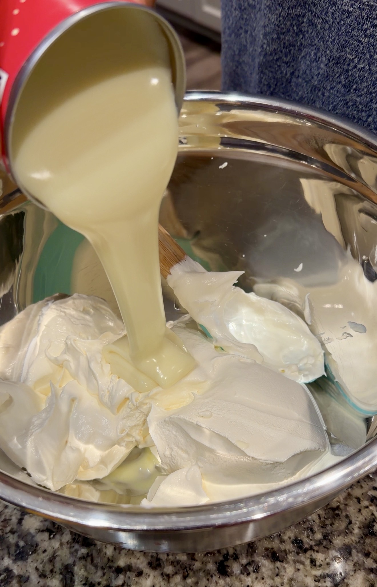 Sweetened condensed milk being poured over Cool Whip in a mixing bowl to make a creamy banana pudding base.