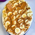 Finished banana pudding topped with banana slices, crushed cookies, whole Biscoff biscuits, and cookie butter drizzle.