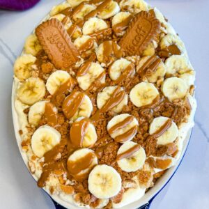 Finished banana pudding topped with banana slices, crushed cookies, whole Biscoff biscuits, and cookie butter drizzle.
