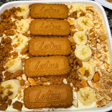 Overhead view of Biscoff banana pudding layered with sliced bananas, crushed Biscoff cookies, and whole Lotus Biscoff biscuits arranged on top in a white baking dish.