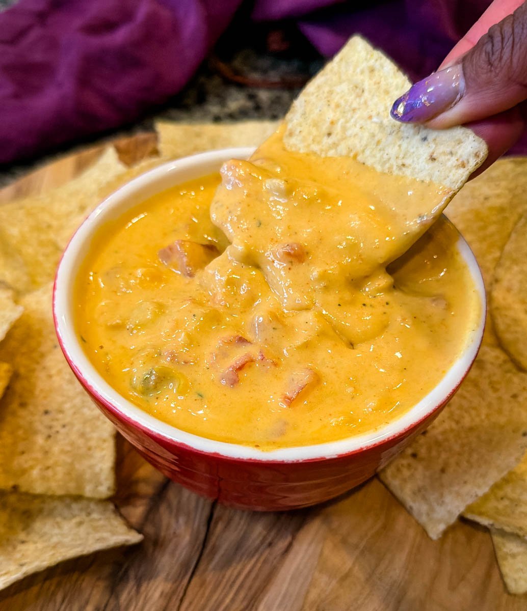 Hand dipping a tortilla chip into a bowl of Chicken Rotel cheese dip without Velveeta, highlighting the creamy queso-style sauce with diced tomatoes and chiles.