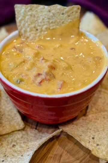 Close-up overhead shot of a bowl of creamy Chicken Rotel Dip without Velveeta, surrounded by tortilla chips, showcasing a smooth cheese sauce with visible tomatoes and green chiles. Text overlay reads “Chicken Rotel Dip without Velveeta.”