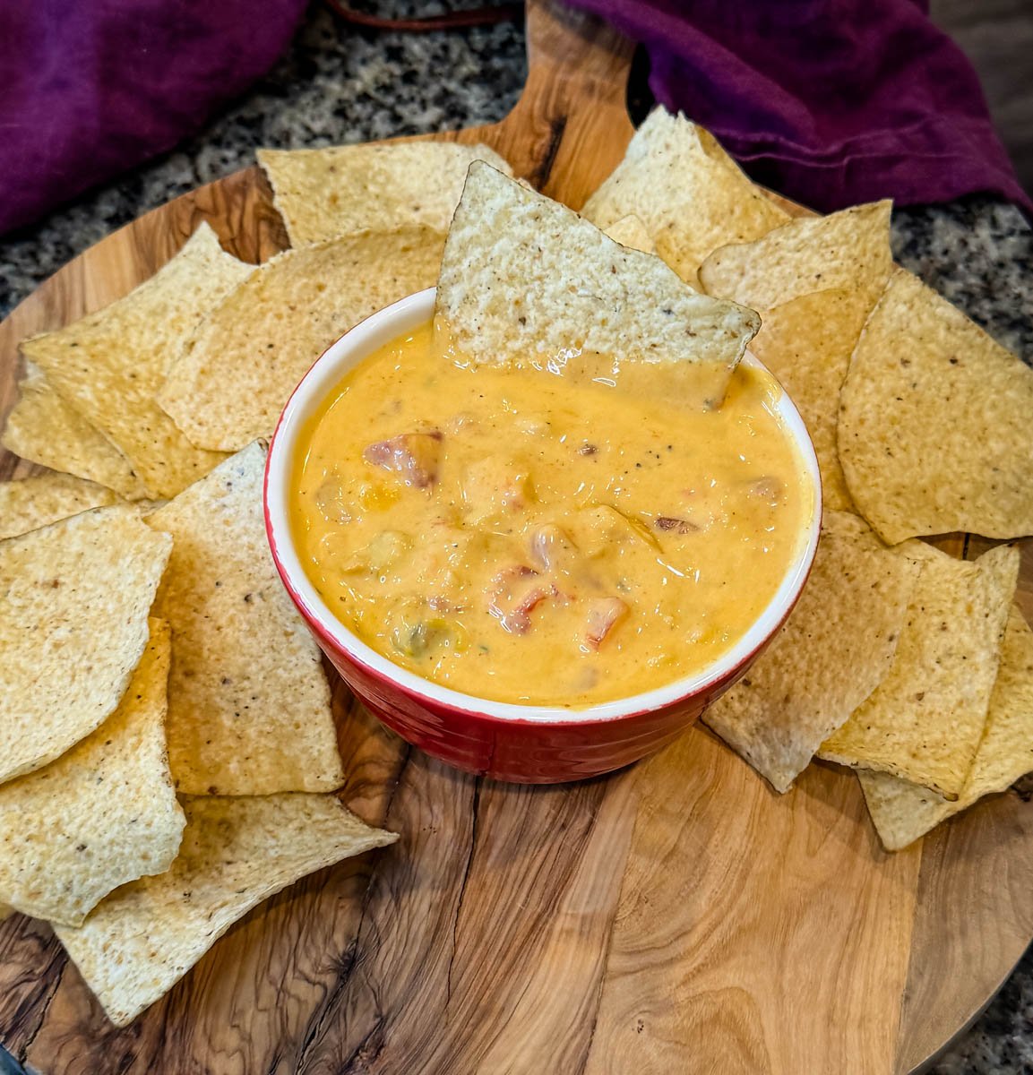 Overhead shot of Chicken Rotel cheese dip served in a red bowl on a wooden board, surrounded by tortilla chips for dipping.