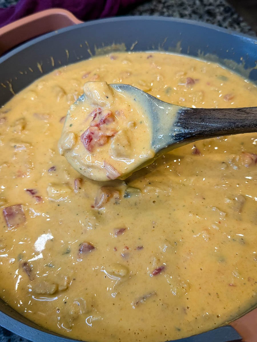 Spoon scooping up Chicken Rotel cheese dip from a skillet, showing the thick, creamy texture and visible diced tomatoes, chiles, and chicken.