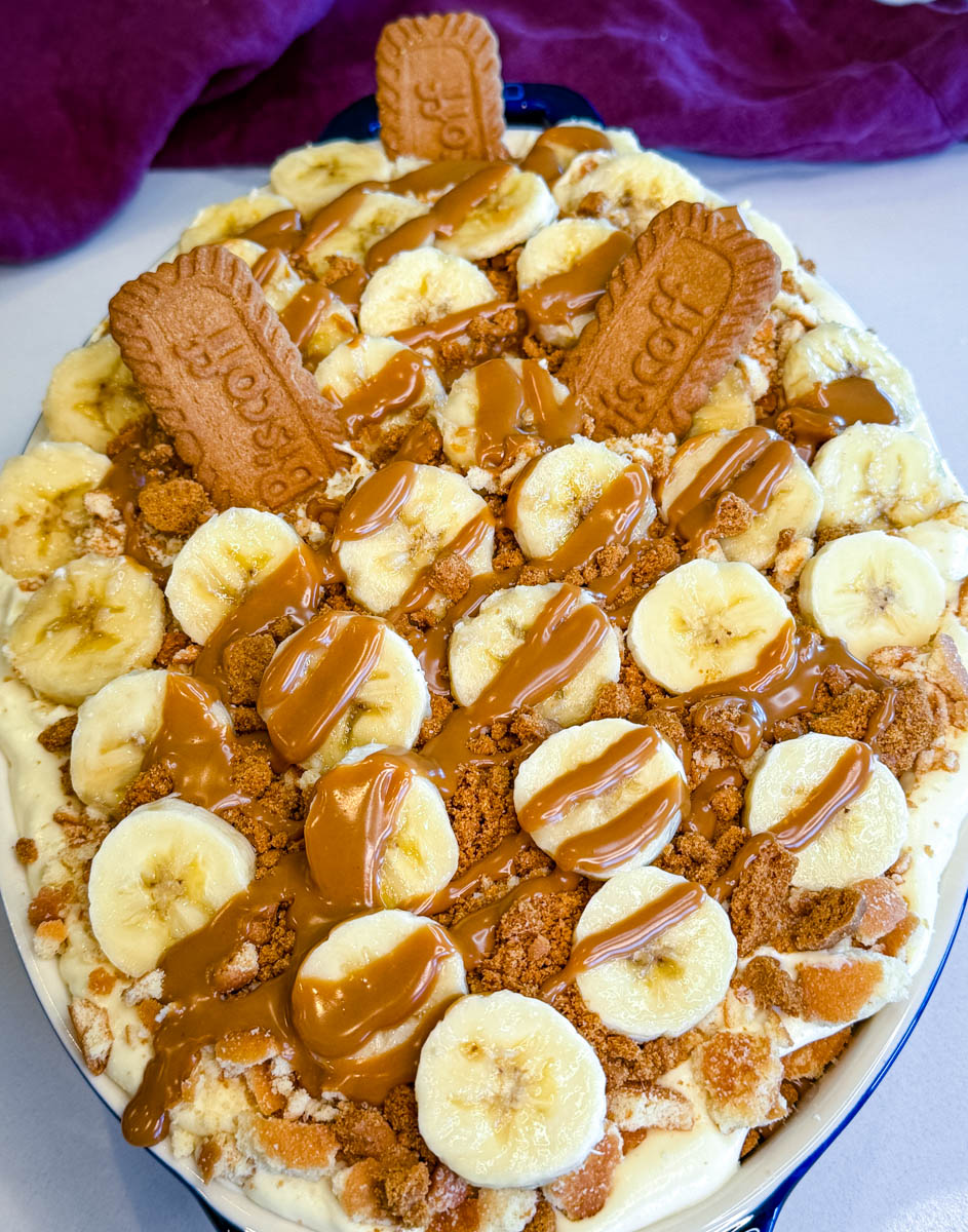 Layer of banana slices and crushed cookies added over creamy pudding in a casserole dish.