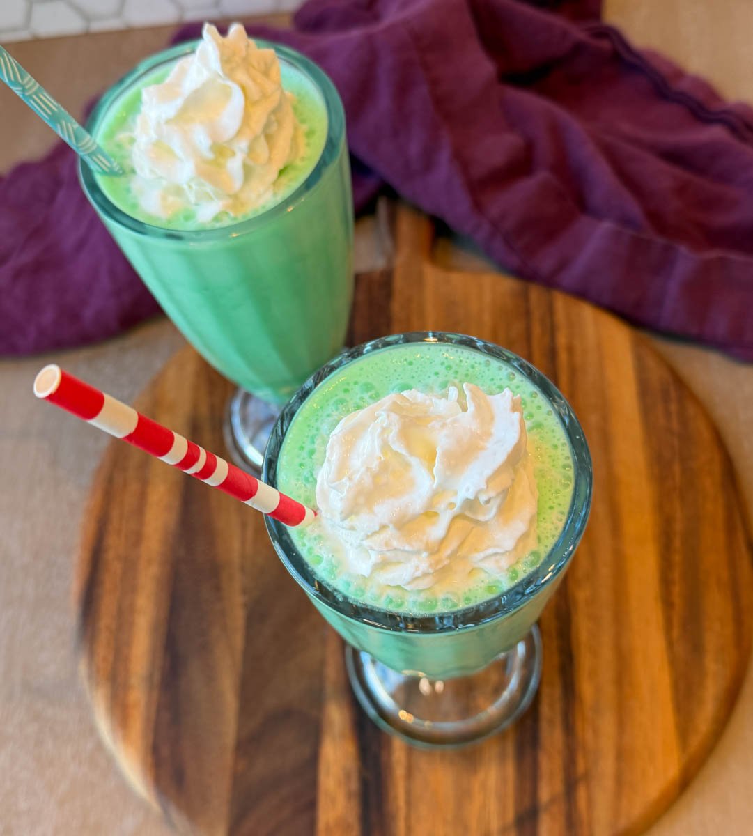 Overhead view of creamy green shamrock shakes with whipped cream and striped straws.