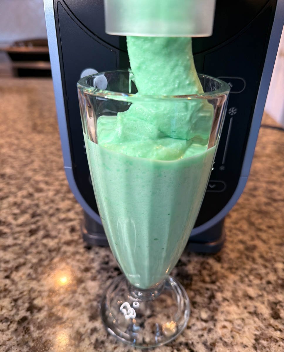 Mint green shamrock shake dispensing thick frozen mixture from a Ninja Slushi machine into a glass.