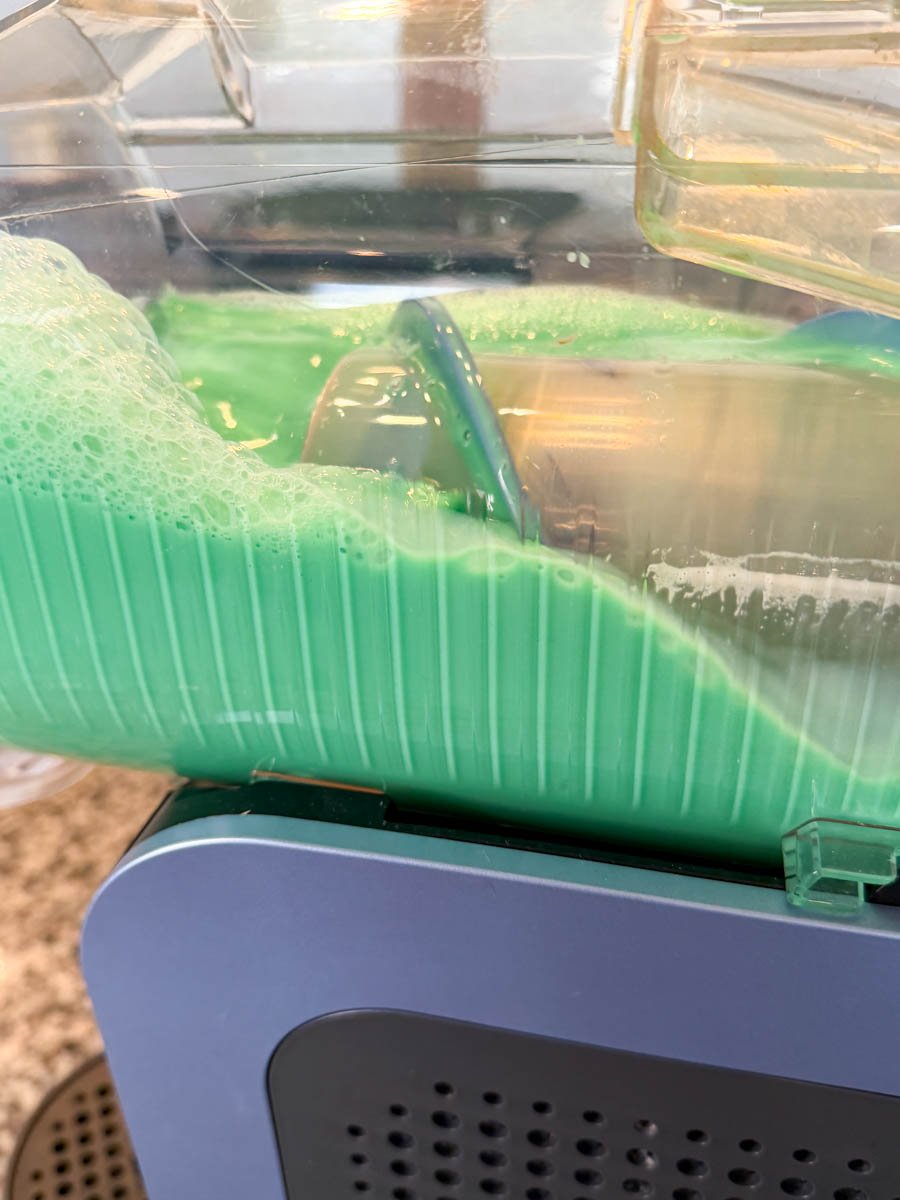 Green shake mixture forming slushy layers while freezing inside the Ninja Slushi maker.