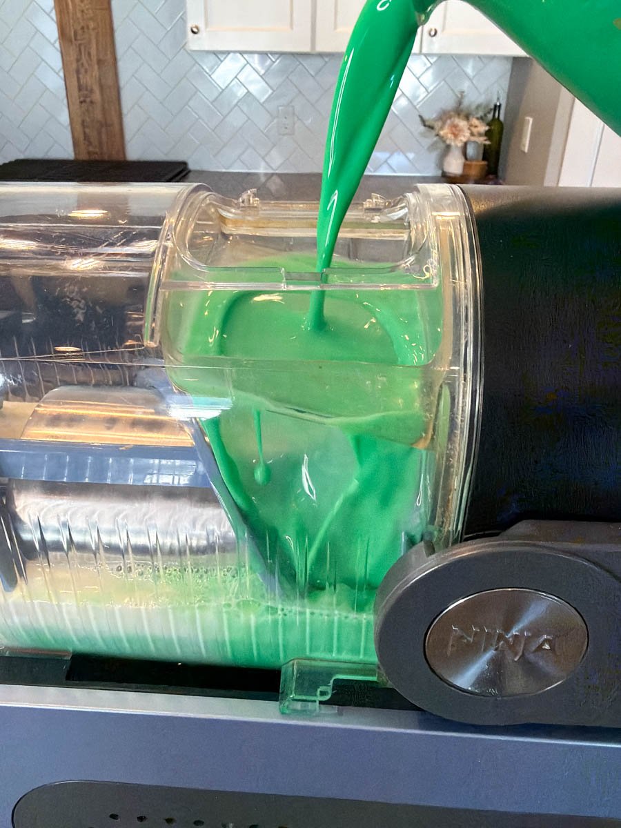 Pouring bright green shamrock shake mixture into a Ninja Slushi machine container.