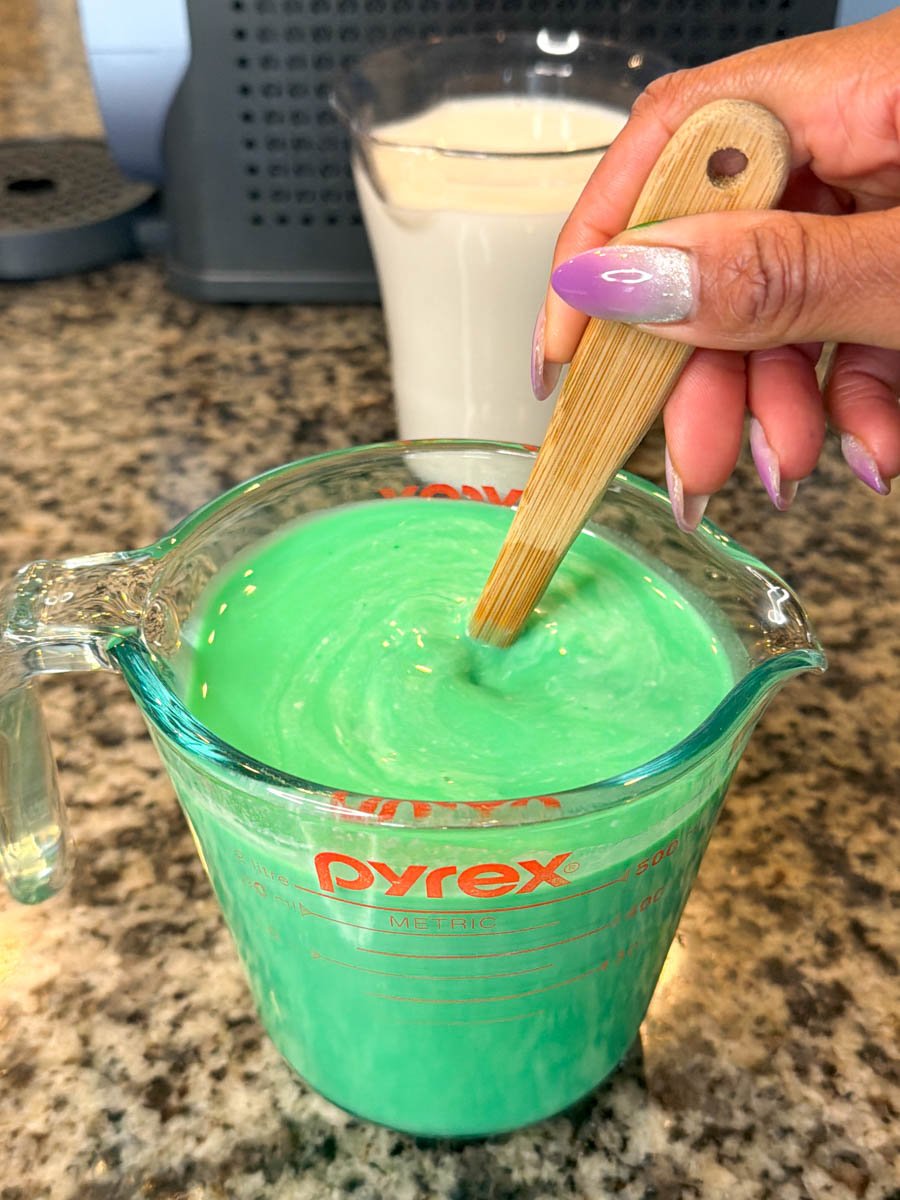 Hand stirring thick mint green shake mixture in a Pyrex measuring cup.