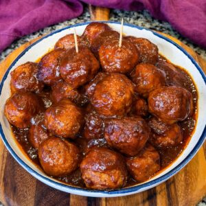 BBQ baby shower meatballs coated in a thick glossy sauce served in a bowl with toothpicks.