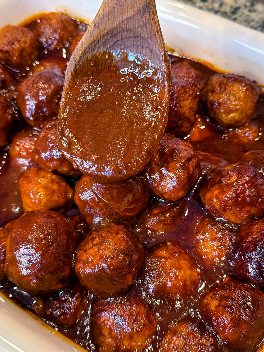 Spoon lifting thick BBQ sauce over baked meatballs