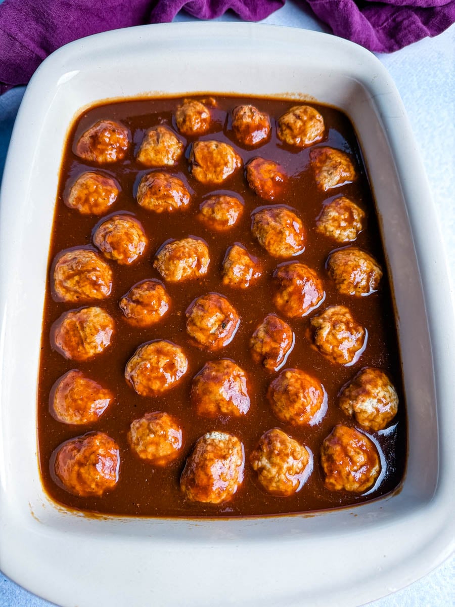 Meatballs arranged in a baking dish covered in rich BBQ sauce before baking