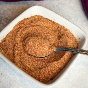White square bowl filled with homemade all purpose seasoning, featuring a smooth, well-mixed spice blend and a metal spoon.