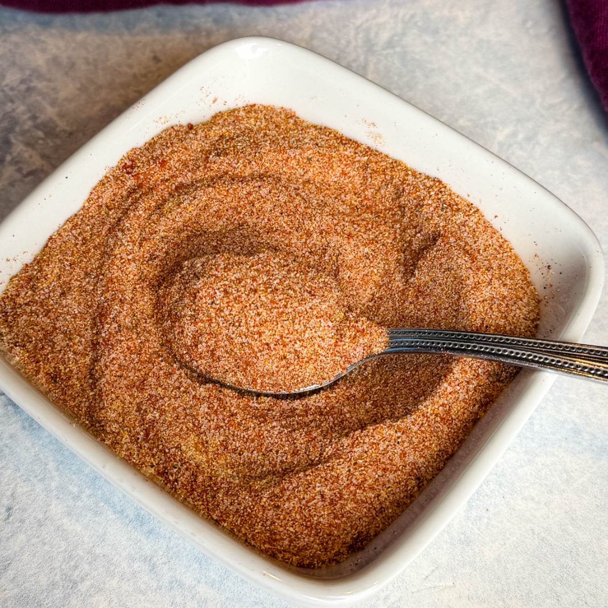 White square bowl filled with homemade all purpose seasoning, featuring a smooth, well-mixed spice blend and a metal spoon.