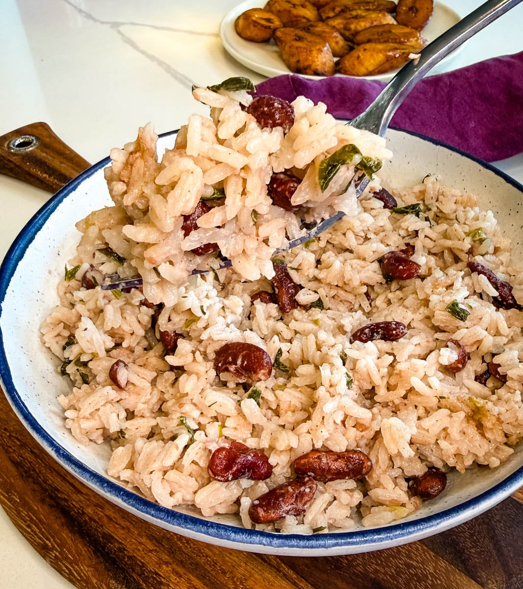 Close-up of fluffy Jamaican rice and peas with red kidney beans and herbs being served with a fork.