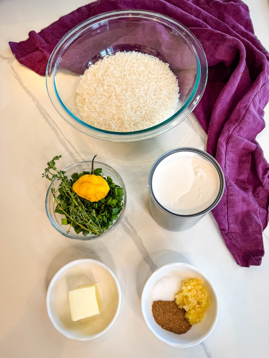 Ingredients for Jamaican rice and peas including uncooked rice, coconut milk, green onions, thyme, garlic, butter, seasoning, and a scotch bonnet pepper.