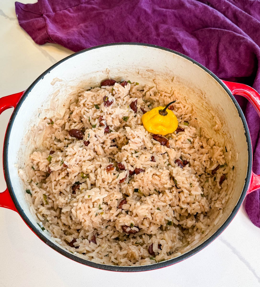 Jamaican rice and peas cooking in a pot with a whole scotch bonnet pepper, kidney beans, and seasoned coconut rice.