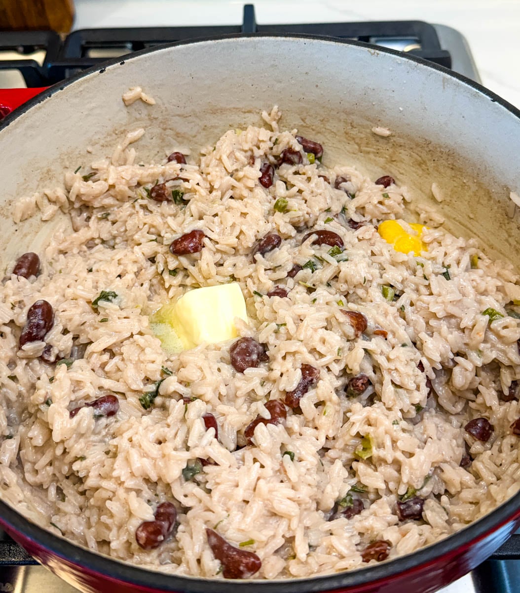 Rice and peas simmering in a pot with butter melting into coconut rice, kidney beans, and herbs.