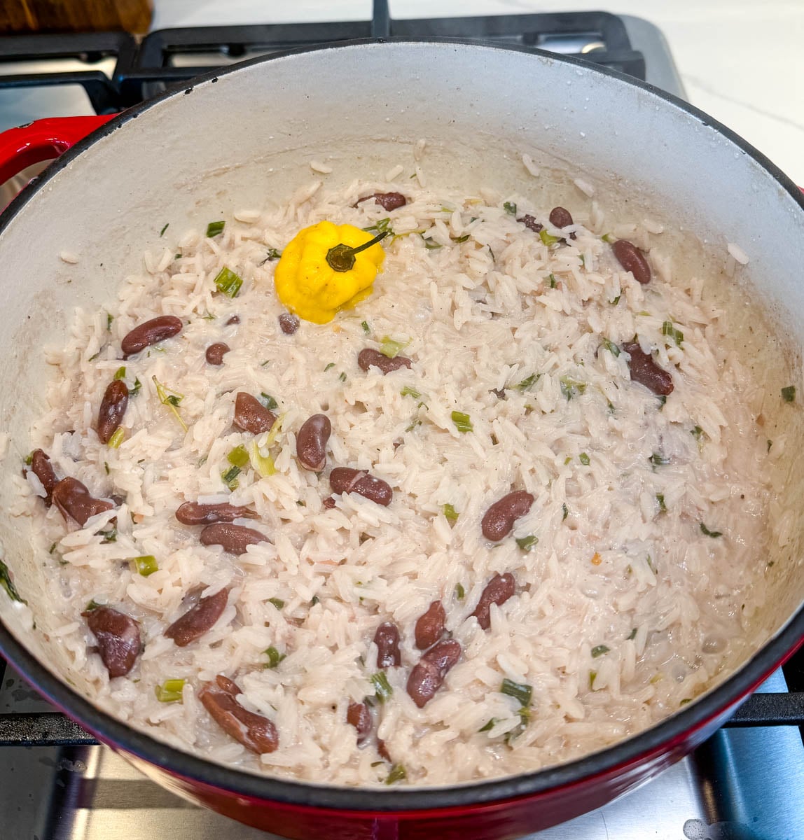Rice and peas simmering in coconut milk with kidney beans, green onions, and a whole scotch bonnet pepper in a pot.