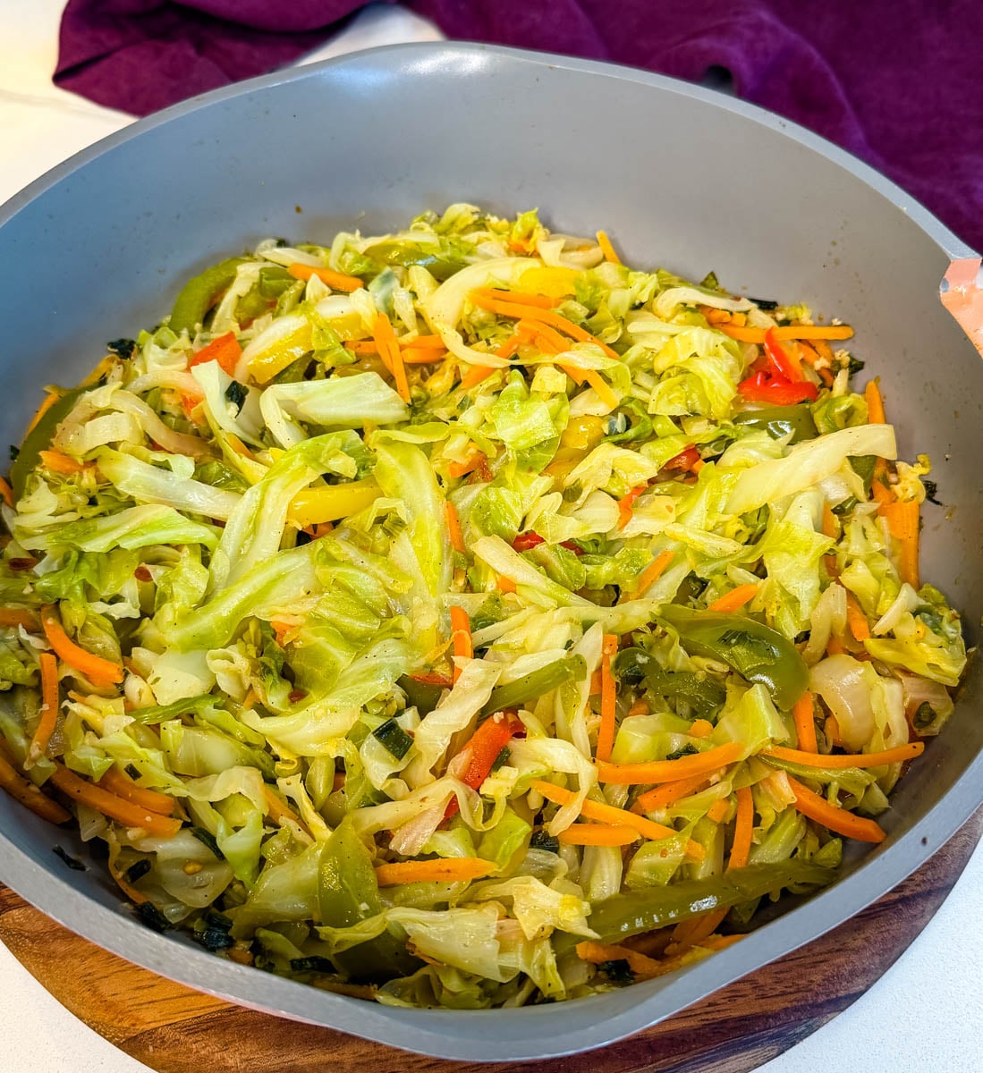 Jamaican steamed cabbage sautéed with bell peppers, carrots, onions, and herbs in a skillet, tender and lightly seasoned.