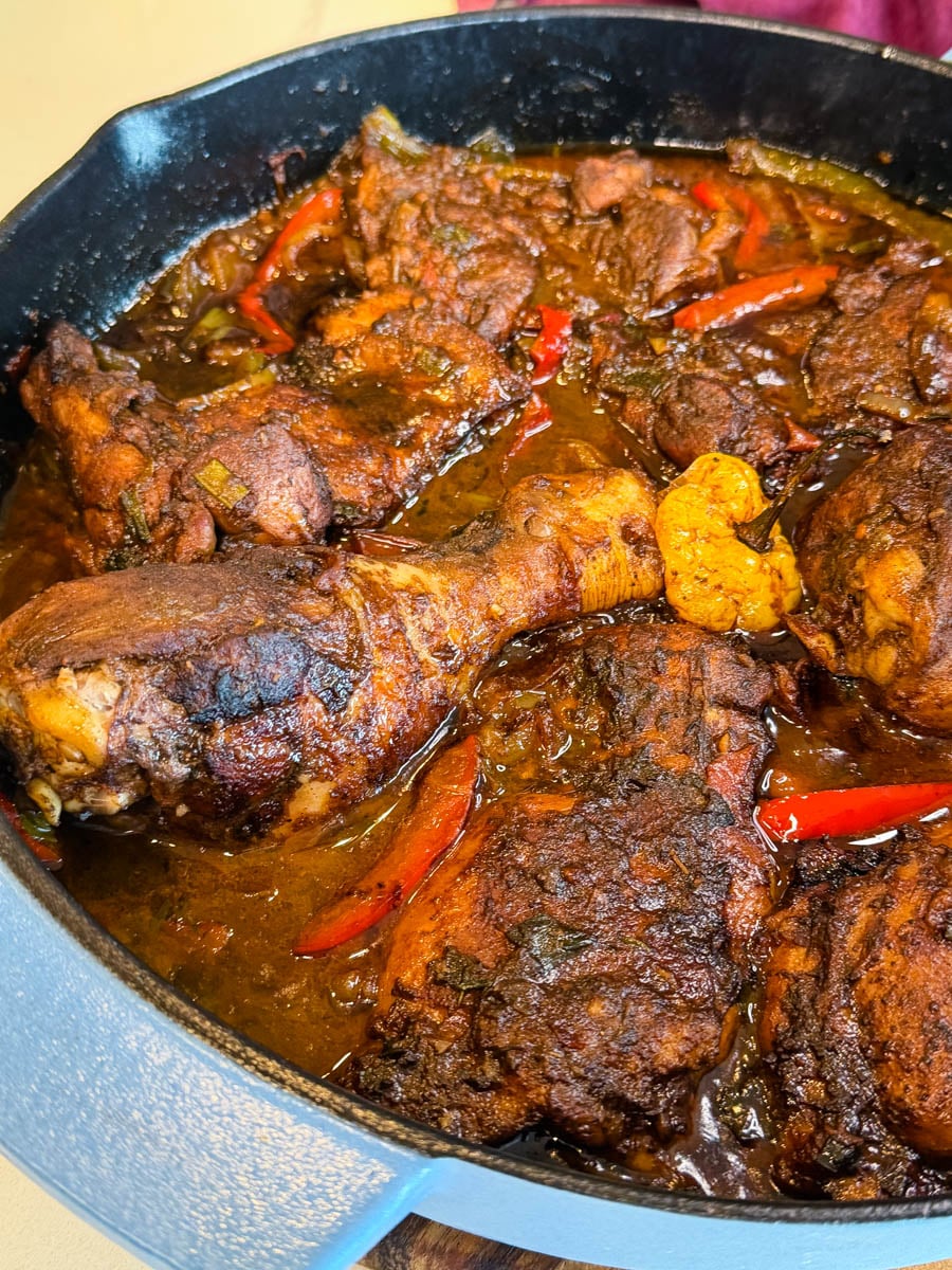 Angled close-up of tender brown stew chicken pieces coated in rich sauce with visible herbs and peppers.