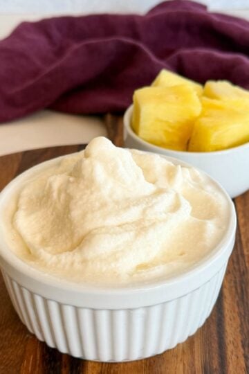 Creamy Ninja Slushi pineapple Dole Whip in a ramekin with fresh pineapple chunks on a wooden board