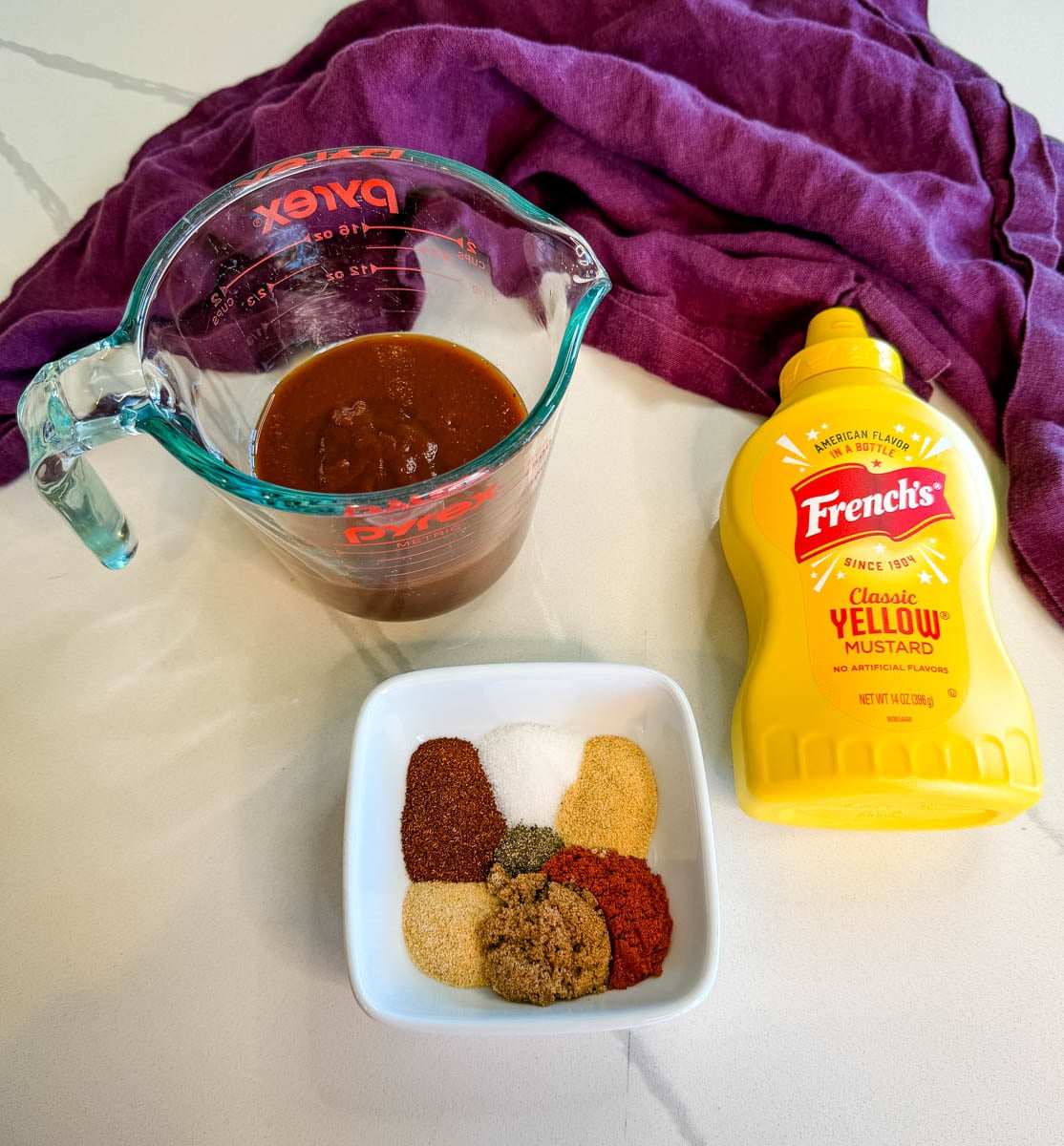 Ingredients for baked beef ribs including BBQ sauce, yellow mustard, and a blend of spices