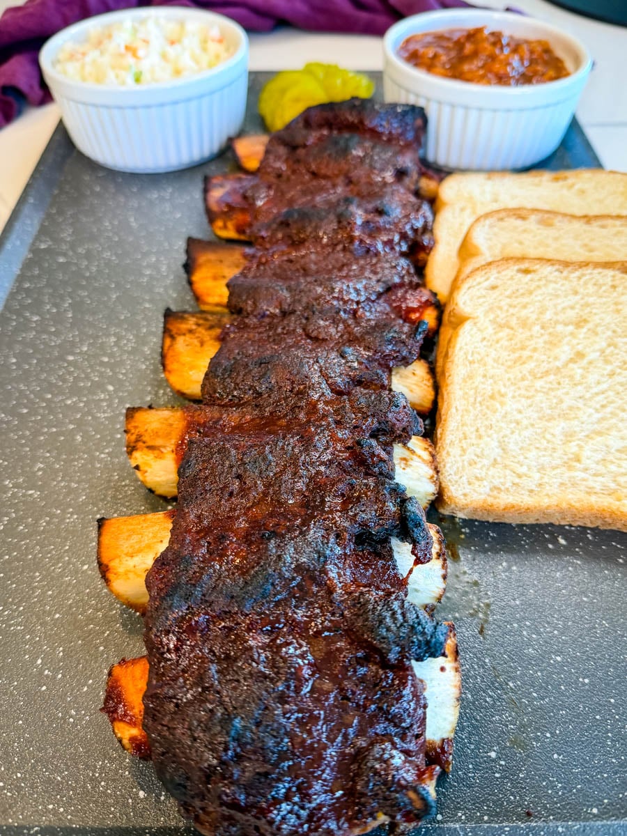 Close-up of tender beef back ribs with a dark, seasoned crust served with classic BBQ sides.