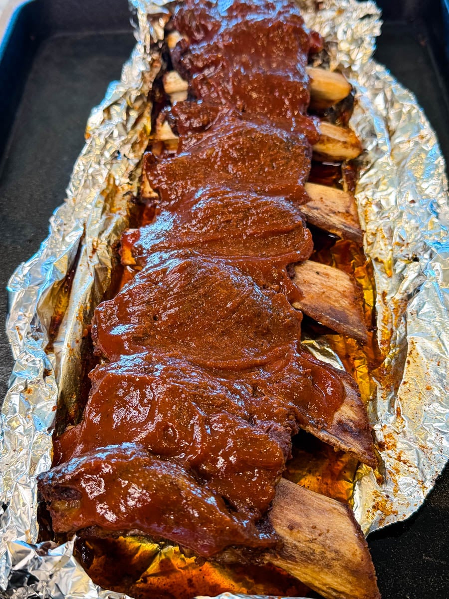Baked beef ribs coated in BBQ sauce resting in foil after cooking.