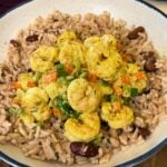Jamaican curry shrimp plated over rice and peas with colorful bell peppers, green onions, and creamy curry sauce in a white bowl.