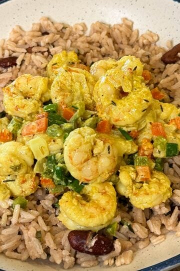 Jamaican curry shrimp plated over rice and peas with colorful bell peppers, green onions, and creamy curry sauce in a white bowl.