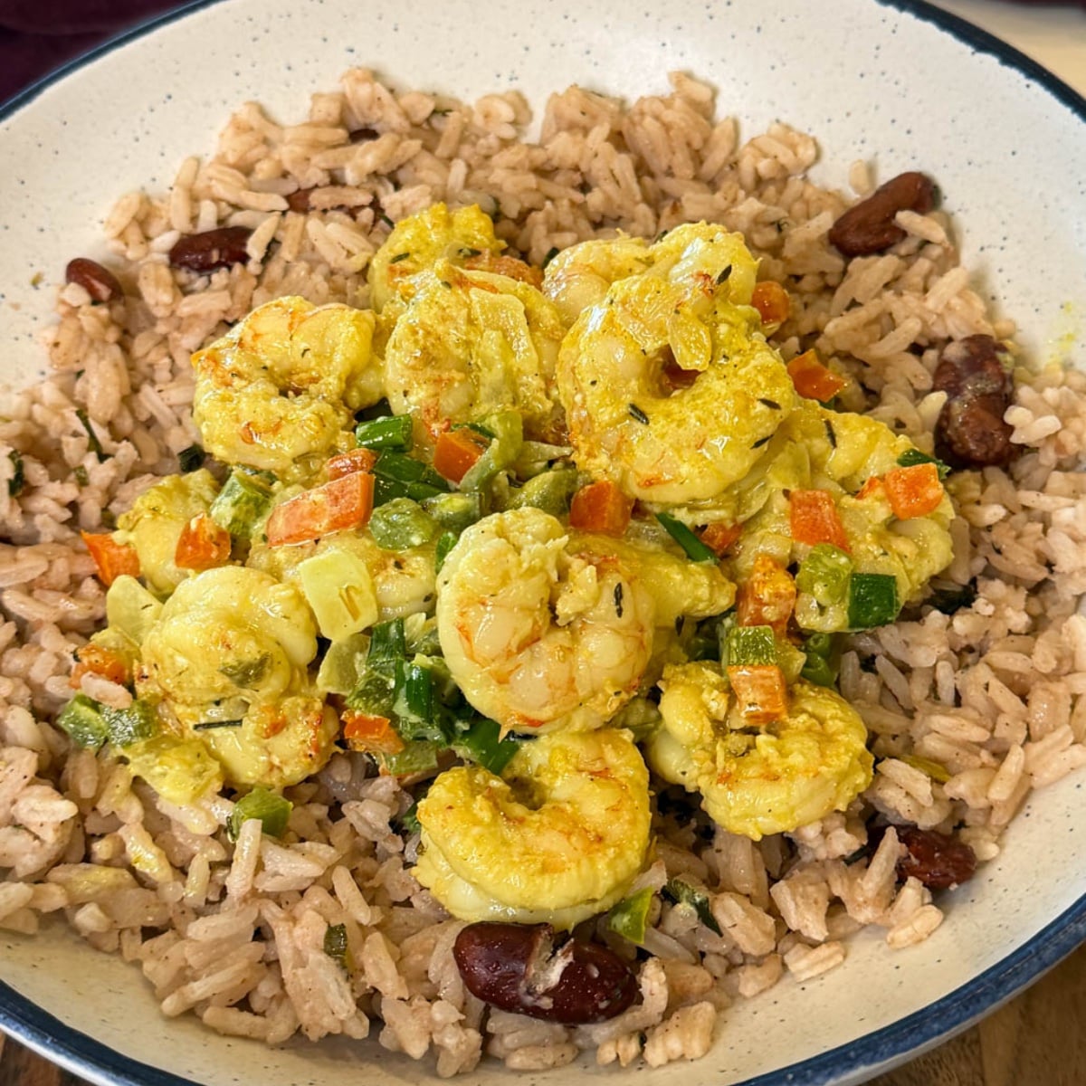 Jamaican curry shrimp plated over rice and peas with colorful bell peppers, green onions, and creamy curry sauce in a white bowl.