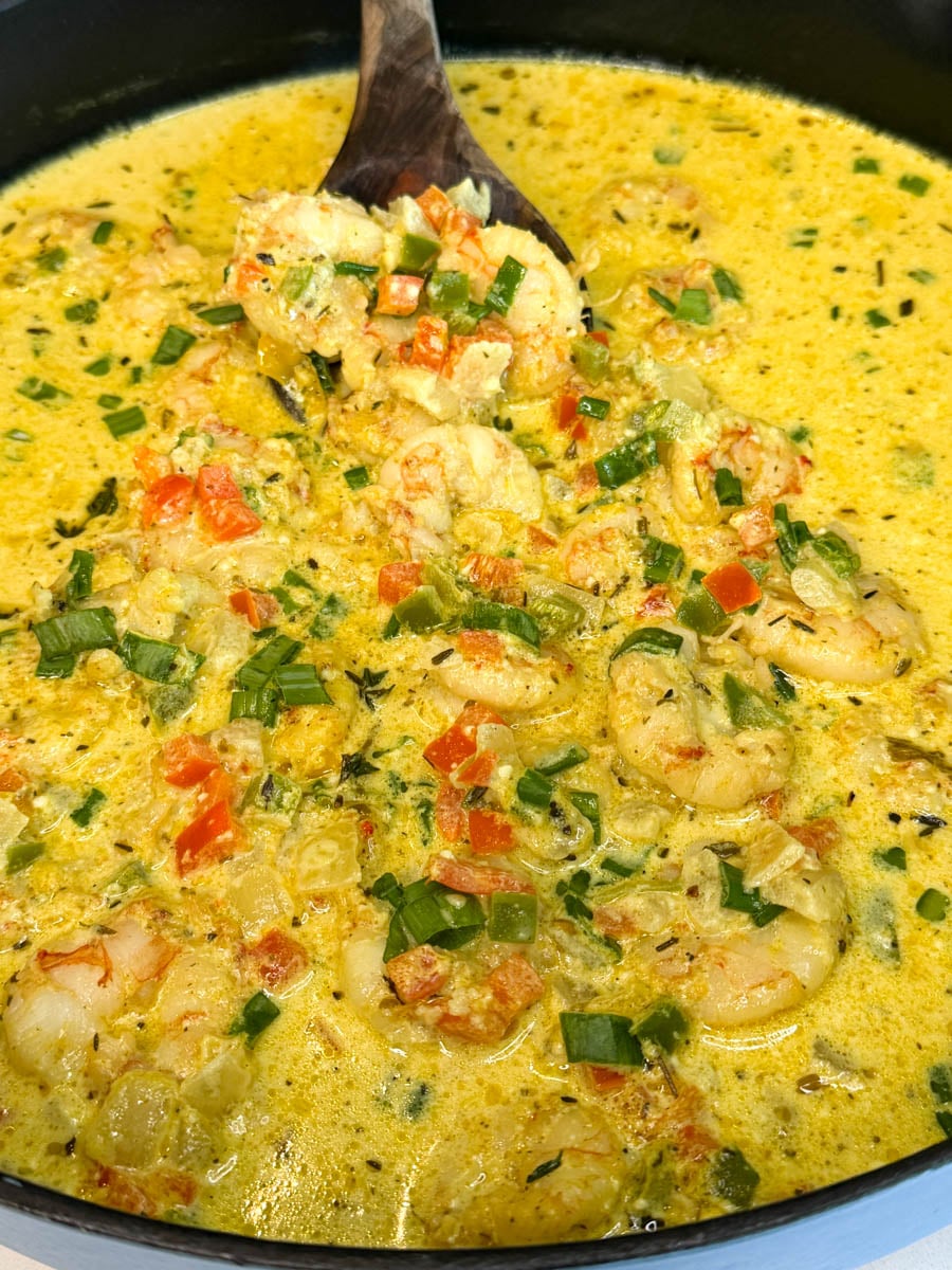 Close-up of Jamaican curry shrimp in rich yellow curry coconut sauce with diced bell peppers, onions, thyme, and fresh green onions garnished on top.