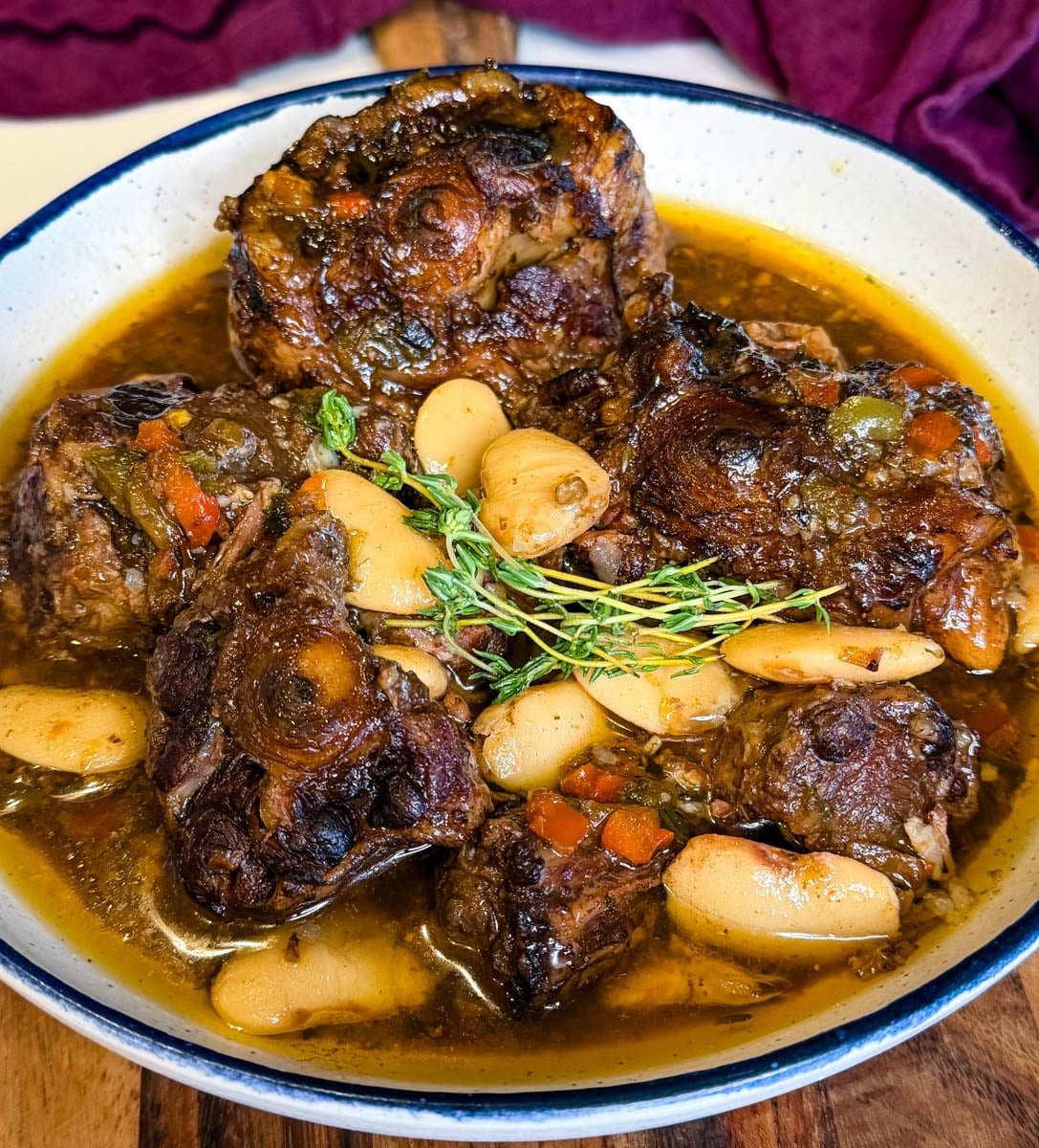 Jamaican oxtail braised in rich brown gravy with butter beans, fresh thyme, and vegetables in a serving bowl.