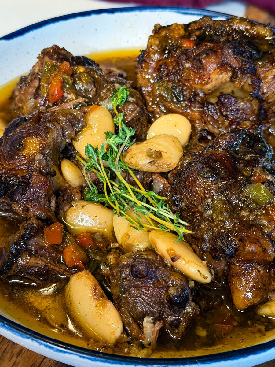 Jamaican oxtail braised until tender and served with butter beans in a flavorful gravy, garnished with fresh thyme.