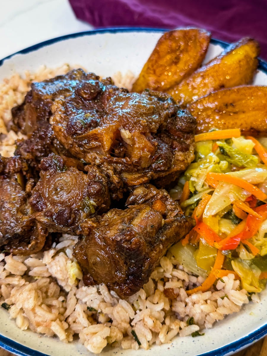 Jamaican oxtail served over rice and peas with fried sweet plantains and steamed vegetables on the side.